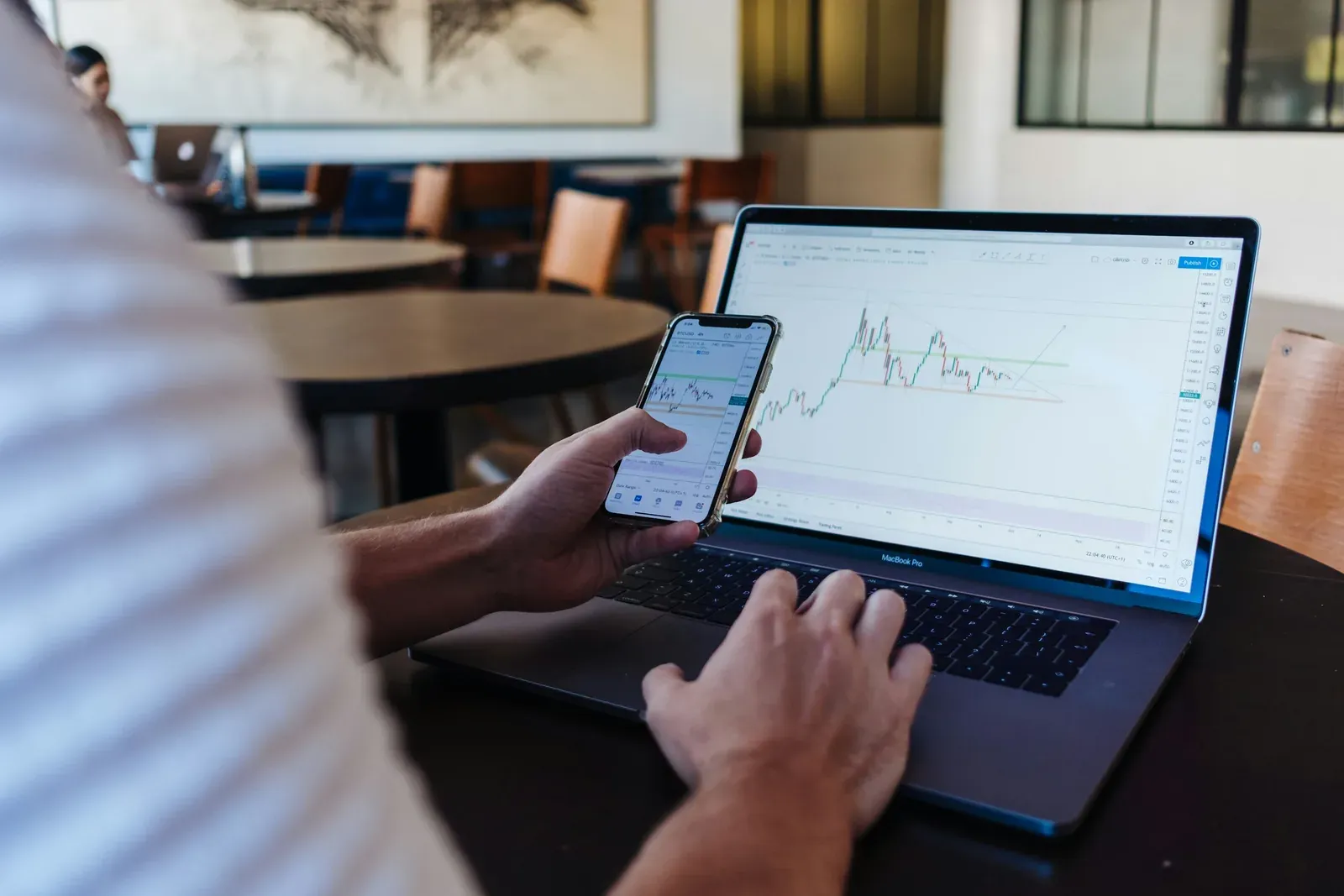 Laptop showing a stock chart alongside a phone in a cafe